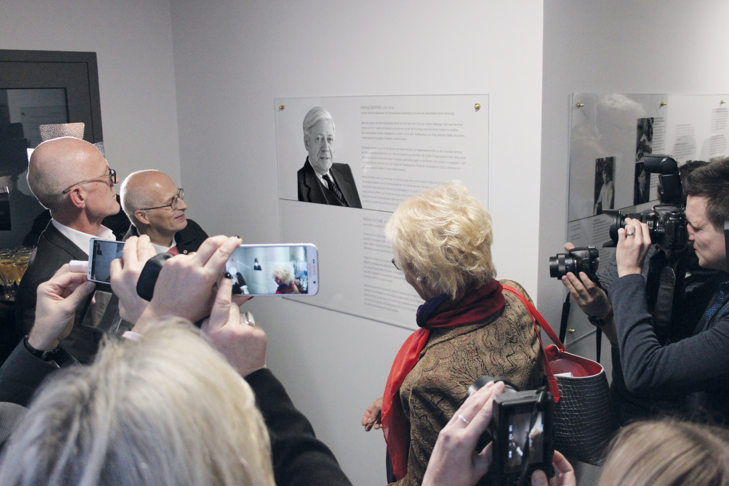 Hamburgs Erster Bürgermeister Peter Tschentscher und Susanne Schmidt vor einer Gedenktafel für Helmut Schmidt. Menschen filmen und fotografieren den Moment.