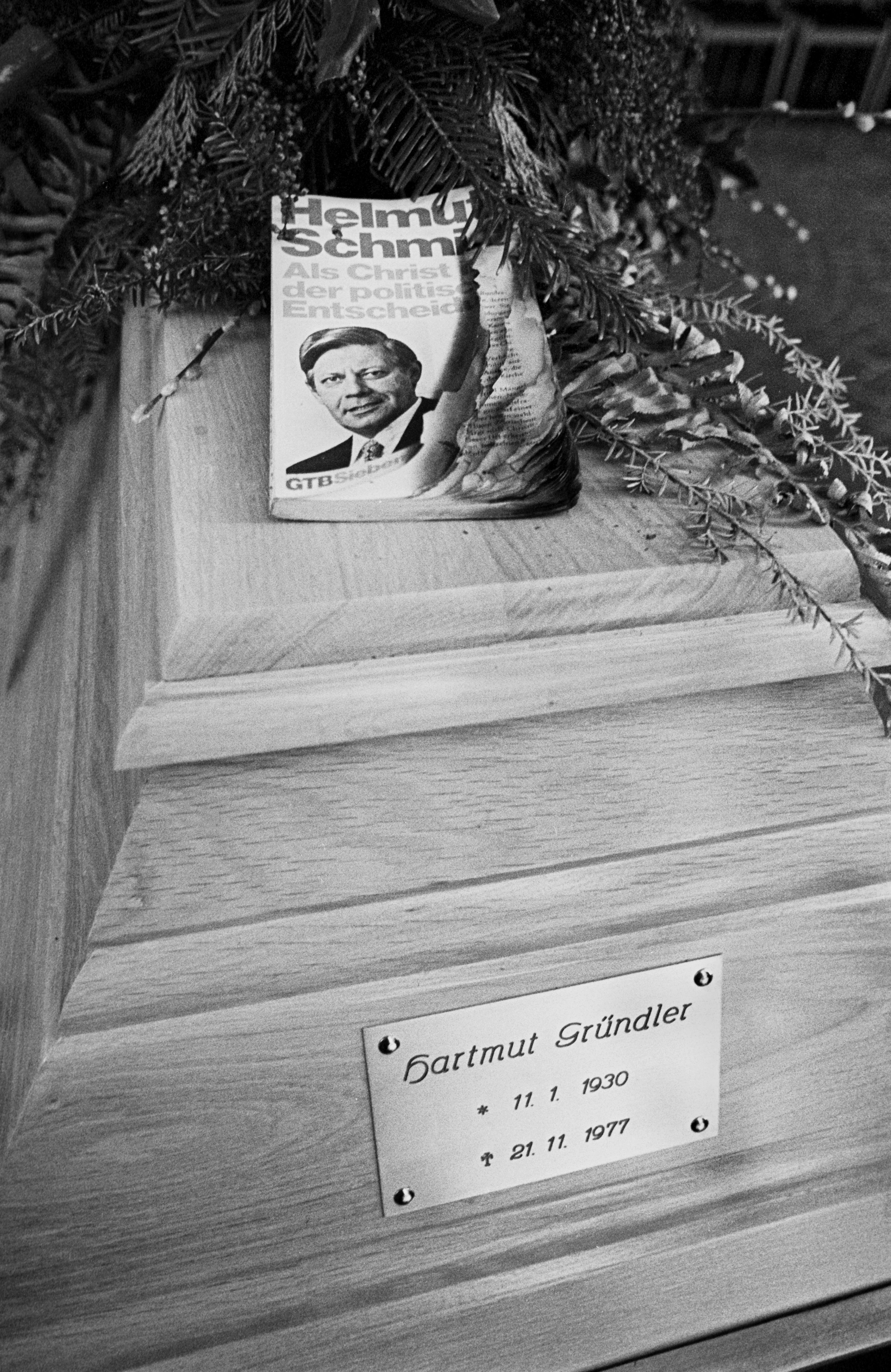 Der Sarg von Hartmut Gründler, darauf platziert eine angebrannte Ausgabe des Buches »Als Christ in der politischen Entscheidung« von Helmut Schmidt.