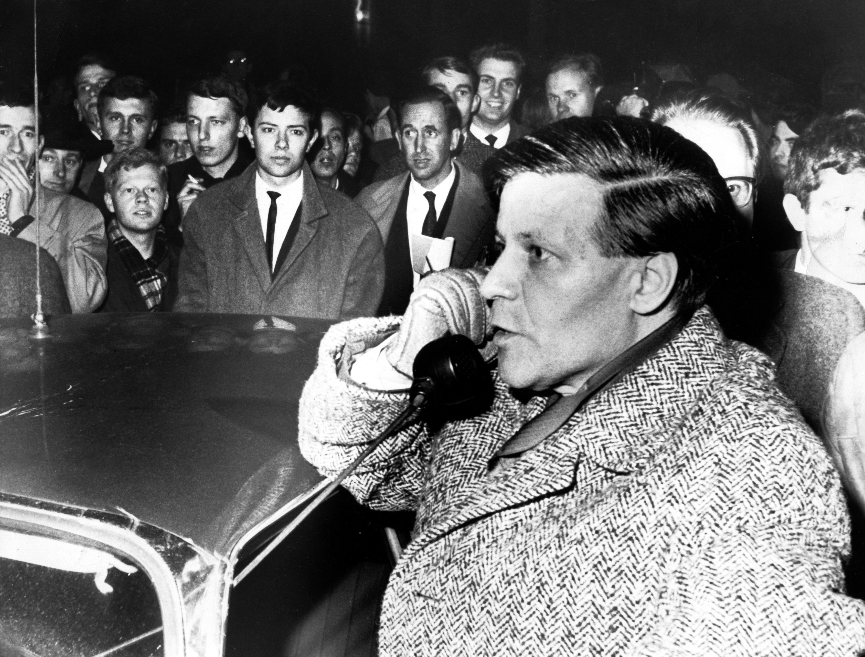 Helmut Schmidt steht an einem Polizeiauto und spricht in den Hörer des Lautsprechers, um ihn herum eine Menschenmenge.