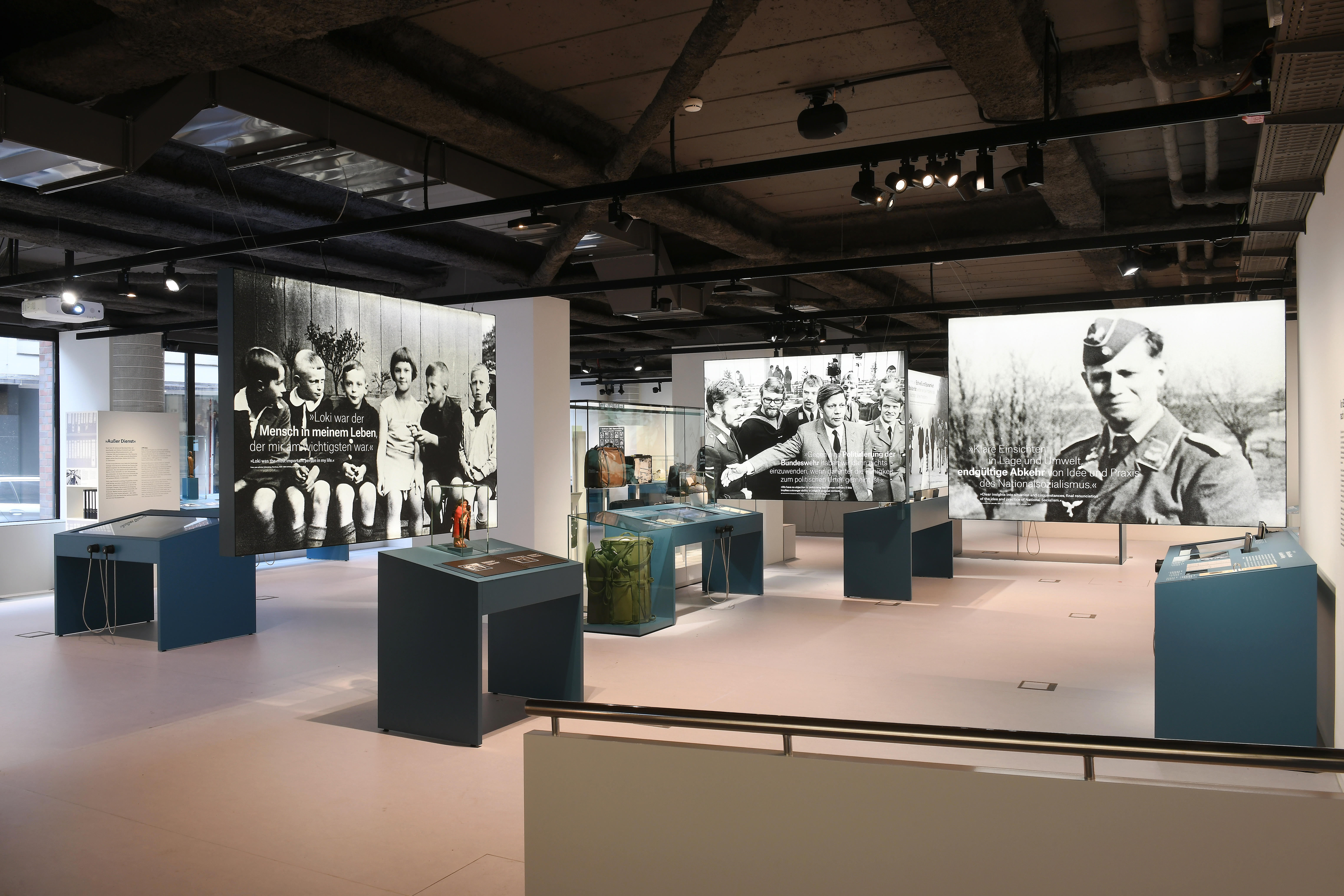 Ansicht des Ausstellungsraums mit Vitrinentischen und großformatigen Bildern.